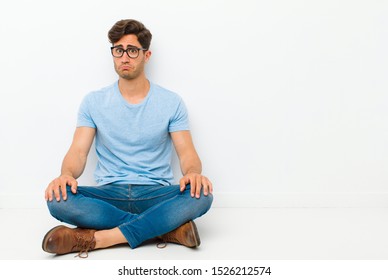 young handsome man feeling sad and stressed, upset because of a bad surprise, with a negative, anxious look sitting on the floor