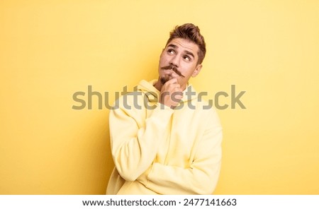 young handsome man feeling thoughtful, wondering or imagining ideas, daydreaming and looking up to copy space. strange moustache concept