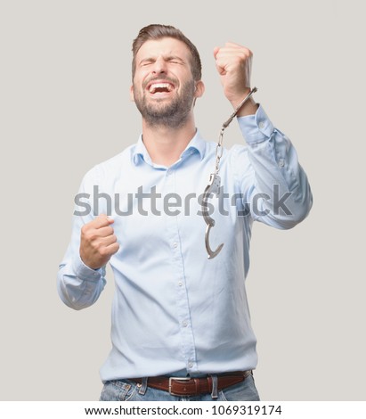 young handsome man with handcuffs celebrating his triumph wearing a blue t shirt . person isolated against monochrome background
