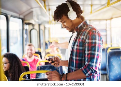 Young handsome man with a headset on is listening to music while looking at his phone and standing on the bus. - Powered by Shutterstock