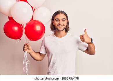 Young handsome man holding balloons smiling happy and positive, thumb up doing excellent and approval sign 