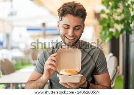 Young handsome man holding a burger with happy expression