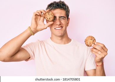 Young handsome man holding cookie winking looking at the camera with sexy expression, cheerful and happy face. 