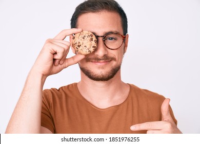 Young handsome man holding cookie pointing finger to one self smiling happy and proud 