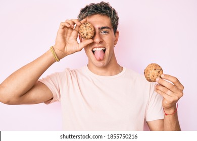 Young handsome man holding cookie sticking tongue out happy with funny expression. 