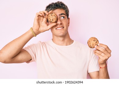 Young handsome man holding cookie smiling looking to the side and staring away thinking. 