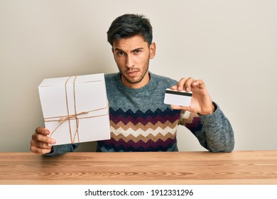 Young Handsome Man Holding Gift And Credit Card Skeptic And Nervous, Frowning Upset Because Of Problem. Negative Person. 