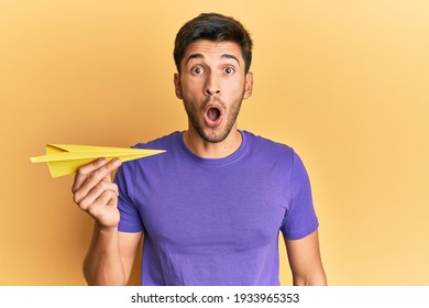 Young Handsome Man Holding Paper Airplane Scared And Amazed With Open Mouth For Surprise, Disbelief Face 