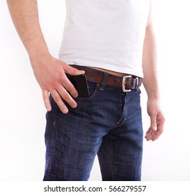 Young Handsome Man In Jeans And Tshirt Putting Cell Phone In Pocket Against White Background