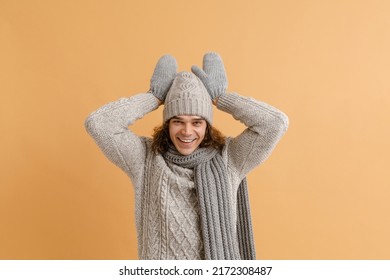 Young Handsome Man With Long Hair In Sweater And Winter Hat, Scarf And Mittens Doing Rabbit Gesture Over Isolated Brown Background