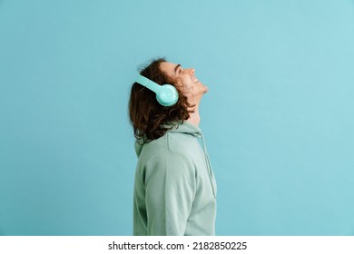 Young handsome man with long hair in hoodie and headphones standing with his right side over isolated blue background - Shutterstock ID 2182850225
