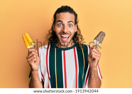 Young handsome man with long hair eating two ice cream celebrating crazy and amazed for success with open eyes screaming excited. 
