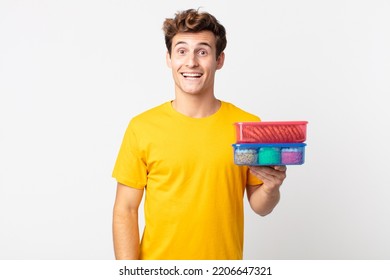 Young Handsome Man Looking Happy And Pleasantly Surprised And Holding Lunch Boxes