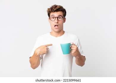 young handsome man looking shocked and surprised with mouth wide open, pointing to self and holding a coffee cup - Powered by Shutterstock