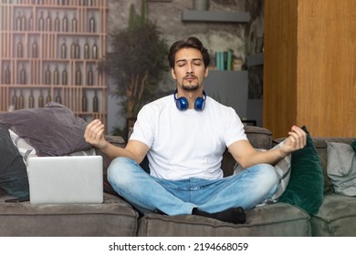 Young Handsome Man Meditating During Break. Freelancer Doing Yoga On Couch After Busy Work Day