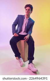 Young handsome man  office clerk  student in jacket   jeans sitting box over light gradient yellow  purple background  Fashion  art  education  business concept  Human emotions