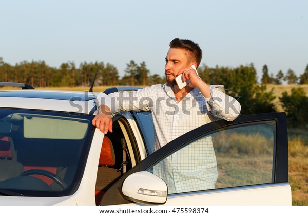 Young handsome man opened the door of\
his car. Man speaks by phone. Always\
connected.