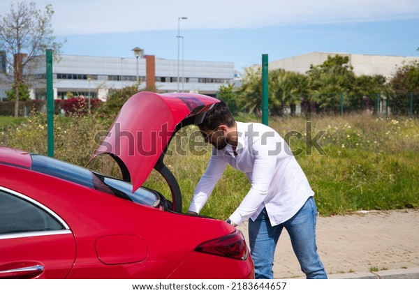 Young, handsome man opens the boot of his\
red sports car. The man is wealthy. High standard of living and\
well positioned\
financially.