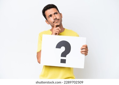 Young handsome man over isolated white background holding a placard with question mark symbol and thinking