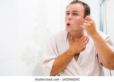 A young handsome man performs a water treatment. He shaves his beard while looking in a bathroom mirror. - Shutterstock ID 1432960292