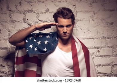 Young handsome man posing with American flag. Saluting like soldier