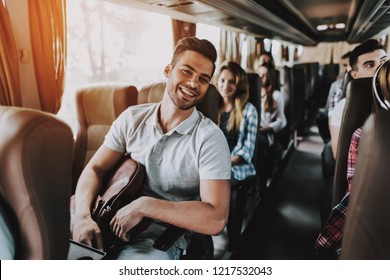 Junge Handsome Mann, die sich im Reisebus-Sitzplatz entspannen. Attraktiver lächelnder Mann sitzend auf Passagiersitz des Touristenbus und Holding-Rucksack. Konzept für Reisen und Tourismus. Fröhliche Reisende auf Reisen