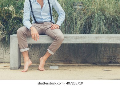 Young handsome man with short hair and beard wearing suspenders and sitting on a concrete bench - Powered by Shutterstock