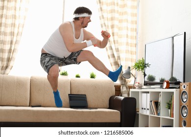 Young handsome man in shorts and vest holds pink dumbbells in hand. Watch tv lessons single combats is practicing receptions of sensei one home fitness indoor training independent education remotely