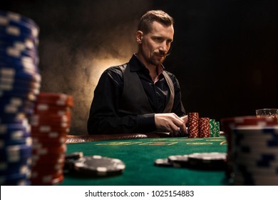 Young handsome man sitting behind poker table with cards and chips