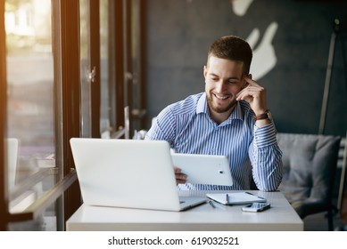 Young handsome man sitting in office with cup of coffee and working on project connected with modern cyber technologies. Businessman with notebook trying to keep deadline in digital marketing sphere. - Powered by Shutterstock