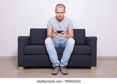 Young Handsome Man Sitting On Sofa With Mobile Phone At Home