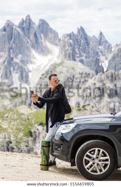 Young handsome\
man sitting on hired car and use on the mobile phone on mountains\
background. Car hire. Car\
trip.