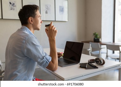 young handsome man sitting at table in co-working office, working at laptop, work place, thinking, drinking coffee in paper cup