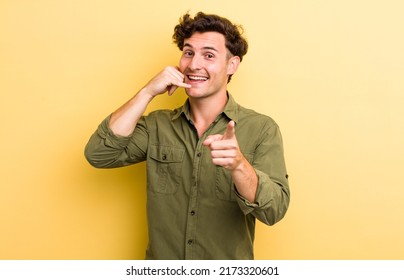 Young Handsome Man Smiling Cheerfully And Pointing To Camera While Making A Call You Later Gesture, Talking On Phone