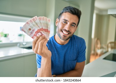 Young handsome man smiling happy holding colombian pesos banknotes at home