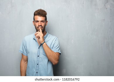 young handsome man smiling, with index finger in front of mouth, requesting silence or sharing a secret - Shutterstock ID 1182016792