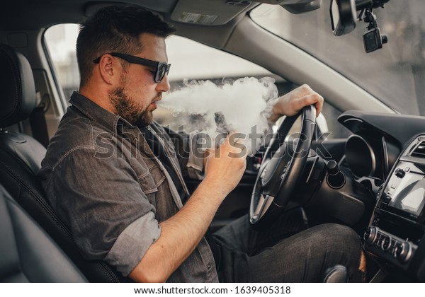 Young handsome
man smoke with vape in
vehicle