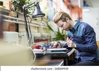 Young handsome man soldering a circuit board and working on fixing hardware - Powered by Shutterstock