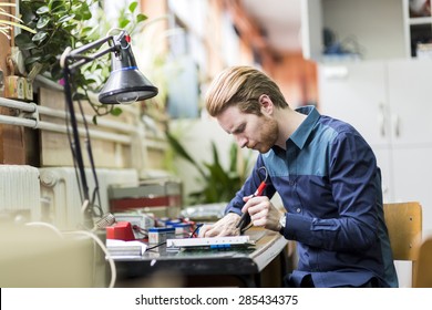 Young handsome man soldering a circuit board and working on fixing hardware