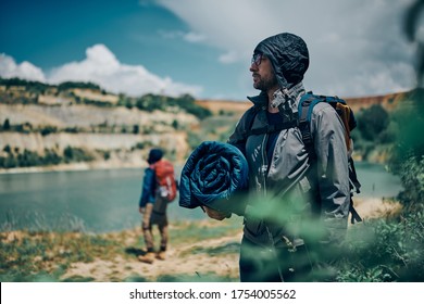 Young Handsome Man Standing In Nature And Searching A Place Where Is Gonna Put Tent And Sleeping Bag. Camping At Weekend Concept.