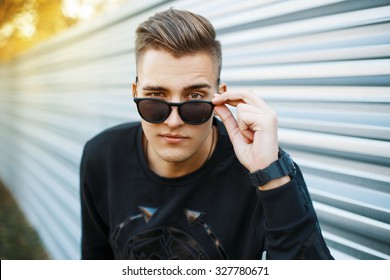 Young handsome man in stylish black clothes looking through sunglasses.