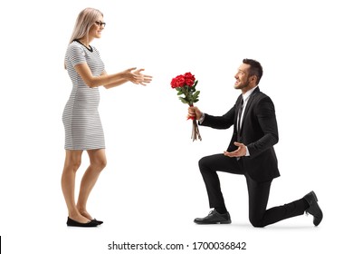 Young Handsome Man In A Suit Kneeling And Giving A Bunch Of Red Roses To A Woman Isolated On White Background