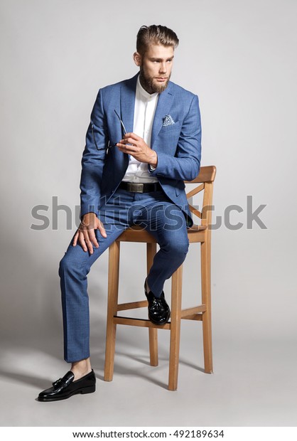 スーツを着た若いハンサムな男性が椅子に座っている の写真素材 今すぐ編集