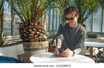 Young Handsome Man In Sunglasses With Phone. White Table. Palm Trees.