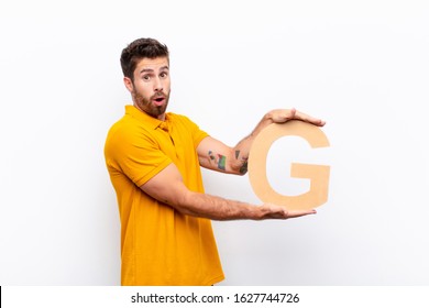 young handsome man surprised, shocked, amazed, holding the letter G of the alphabet to form a word or a sentence.