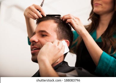 Young Handsome Man Talking Over The Phone While Getting A Haircut In A Barber Shop