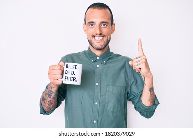 Young Handsome Man With Tattoo Drinking Mug Of Coffe With Best Dad Ever Message Smiling With An Idea Or Question Pointing Finger With Happy Face, Number One 