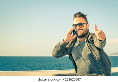 Young handsome man with thumbs up during a phone call with his smartphone - Concept of technology connected with traveller lifestyle - Male model showing success for a mobile telephony company