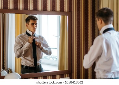 A young handsome man ties up a tie in front of a mirror - Powered by Shutterstock