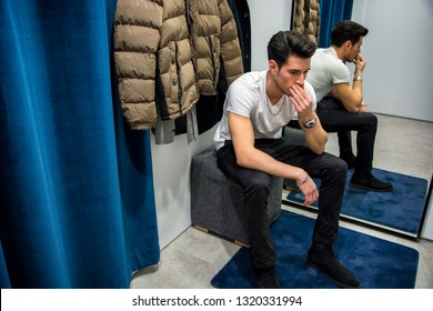 Young Handsome Man Trying On Clothes In Clothing Store's Changing Room In Front Of A Mirror Or In Room Closet